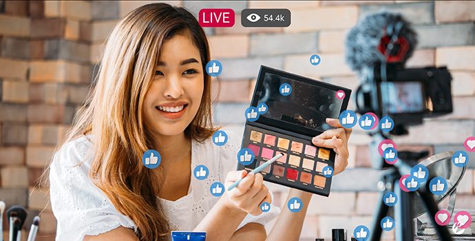 A woman on a live stream holding an eyeshadow palette up to the camera