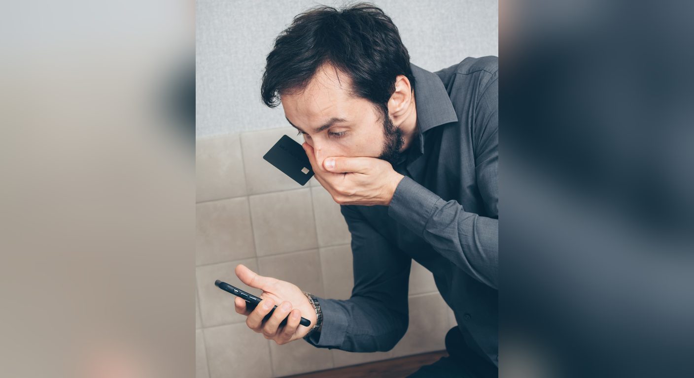 A shopper holding a card and a phone who has just realised he was scammed