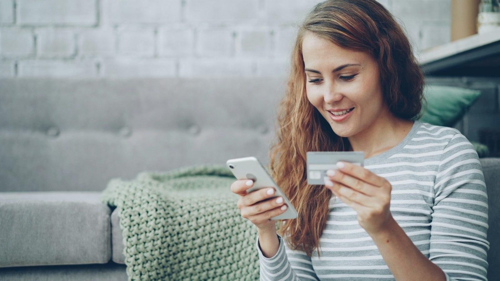 A woman on a sofa paying for an order with her phone and a bank card