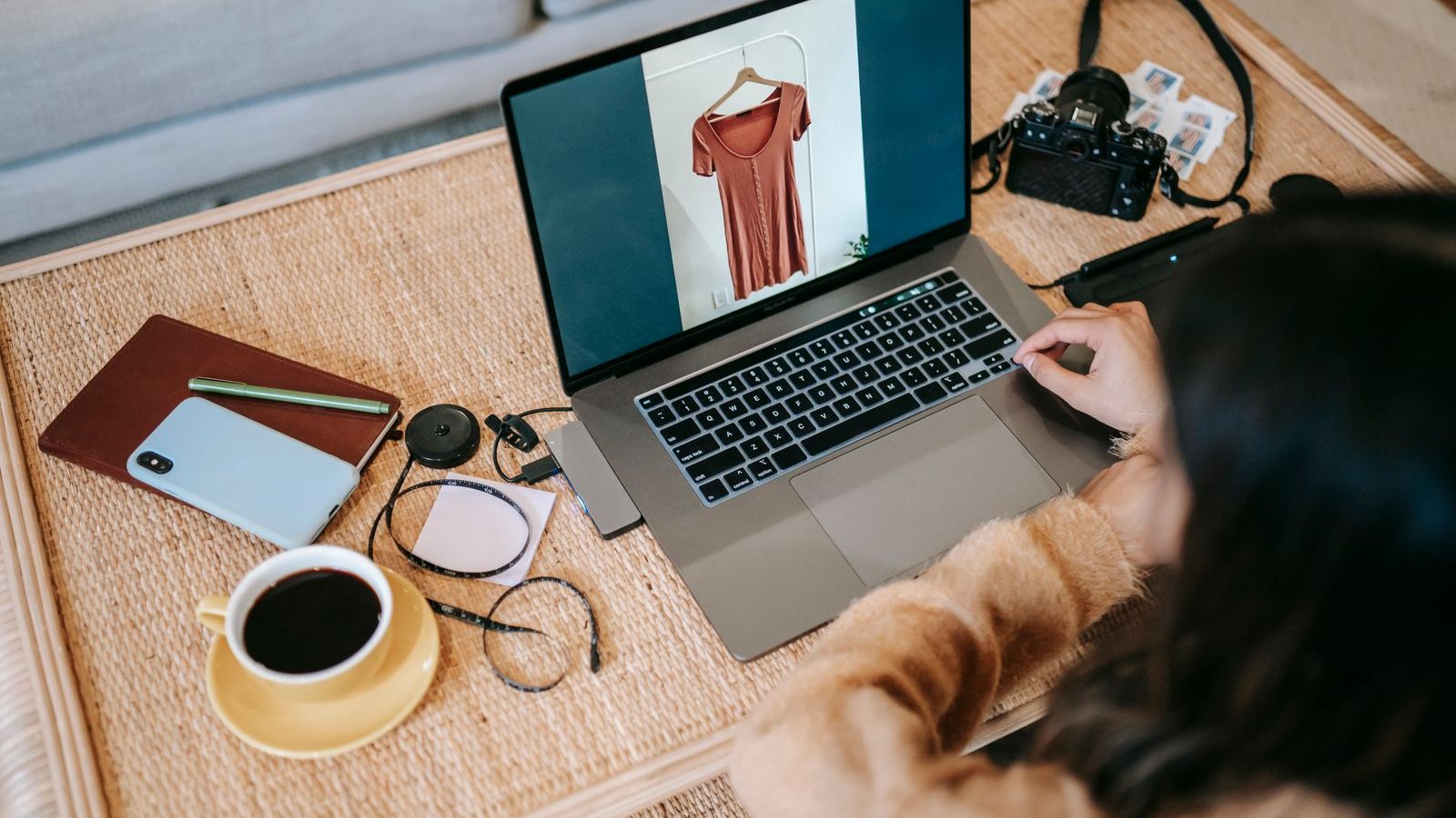A seller reviewing a product photo on a laptop, with a phone, a notebook and a camera on the table